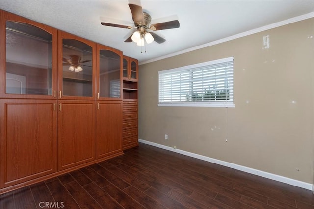 unfurnished room with crown molding, dark wood finished floors, a ceiling fan, and baseboards