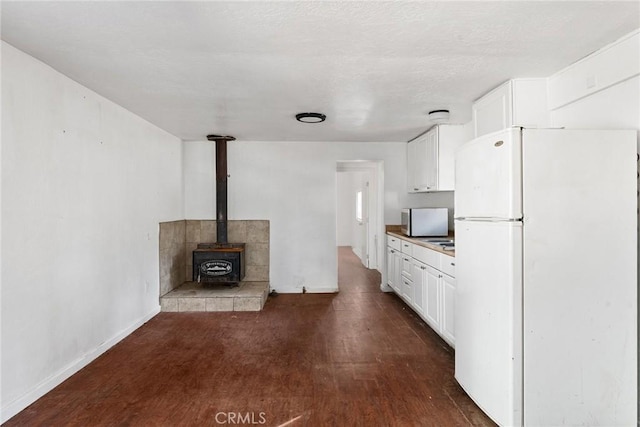 kitchen with hardwood / wood-style flooring, white cabinetry, white fridge, and a wood stove