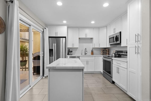 kitchen with appliances with stainless steel finishes, white cabinetry, a kitchen island, a sink, and light stone countertops