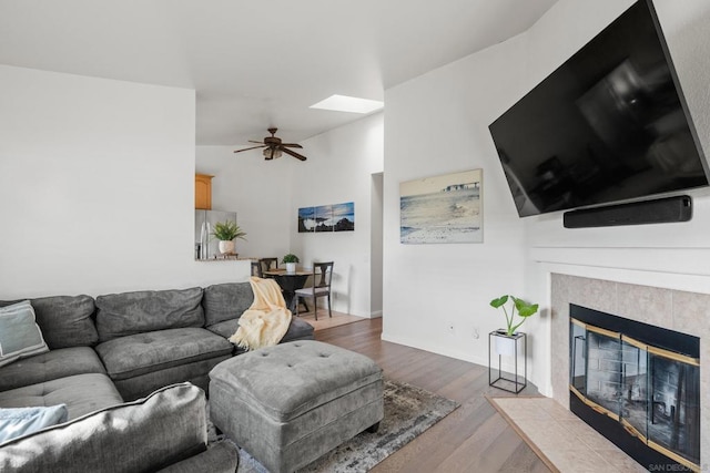 living room with ceiling fan, lofted ceiling with skylight, light hardwood / wood-style floors, and a tile fireplace