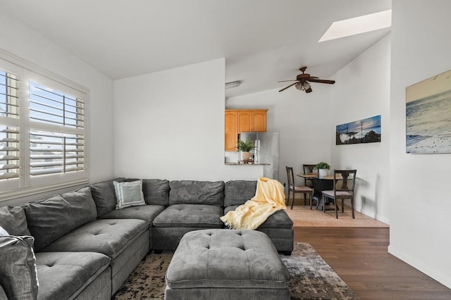 living room with dark wood-type flooring, vaulted ceiling with skylight, and ceiling fan