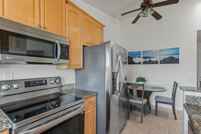 kitchen featuring stainless steel appliances, light tile patterned floors, and dark stone countertops