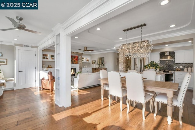 dining area featuring ornamental molding, a fireplace, and light hardwood / wood-style flooring