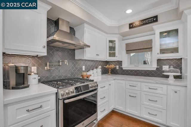 kitchen featuring white cabinetry, crown molding, stainless steel gas range, and wall chimney range hood