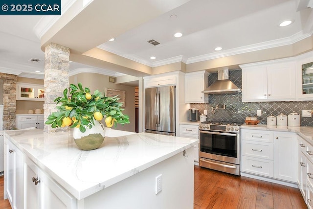 kitchen featuring light stone counters, wall chimney range hood, white cabinets, and appliances with stainless steel finishes