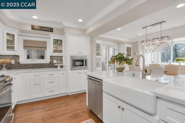 kitchen featuring ornamental molding, stainless steel appliances, decorative light fixtures, and white cabinets