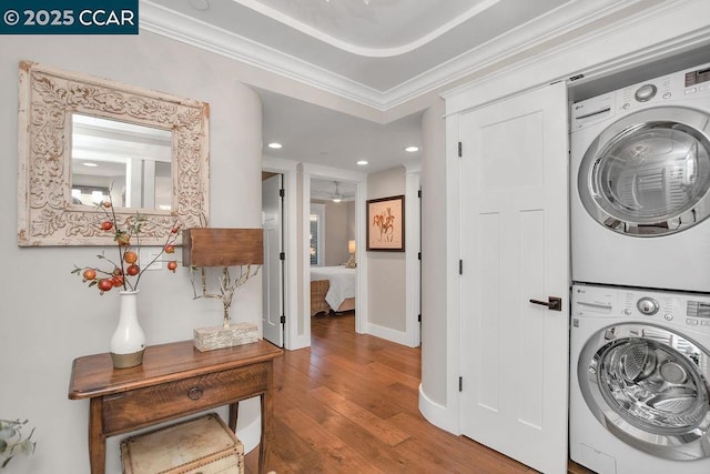 washroom with hardwood / wood-style flooring, crown molding, and stacked washer / drying machine