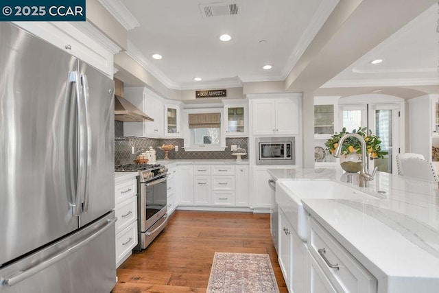 kitchen with crown molding, appliances with stainless steel finishes, white cabinetry, wood-type flooring, and light stone countertops