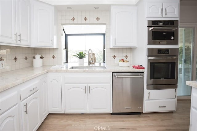 kitchen with sink, white cabinetry, stainless steel appliances, light stone countertops, and backsplash