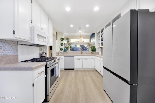 kitchen featuring appliances with stainless steel finishes, tasteful backsplash, white cabinets, an inviting chandelier, and light hardwood / wood-style flooring