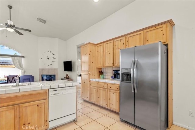 kitchen with stainless steel fridge, tile counters, open floor plan, white dishwasher, and light brown cabinets