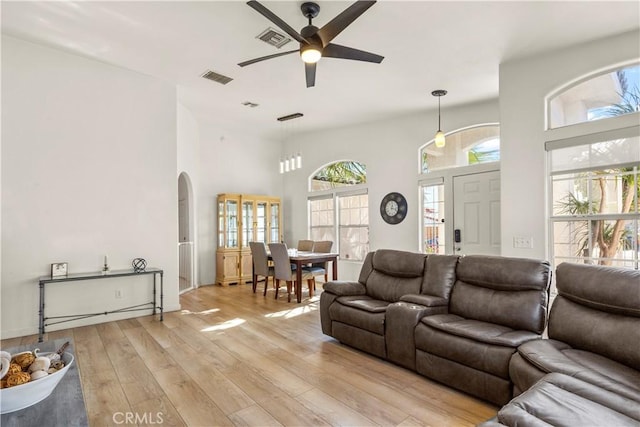 living room with a high ceiling, ceiling fan, and light wood-type flooring