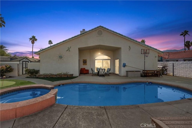 pool at dusk featuring an in ground hot tub and a patio