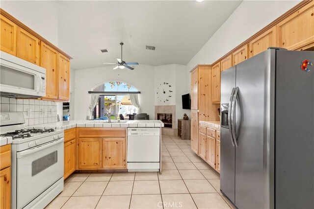 kitchen with light tile patterned flooring, a peninsula, white appliances, visible vents, and a ceiling fan