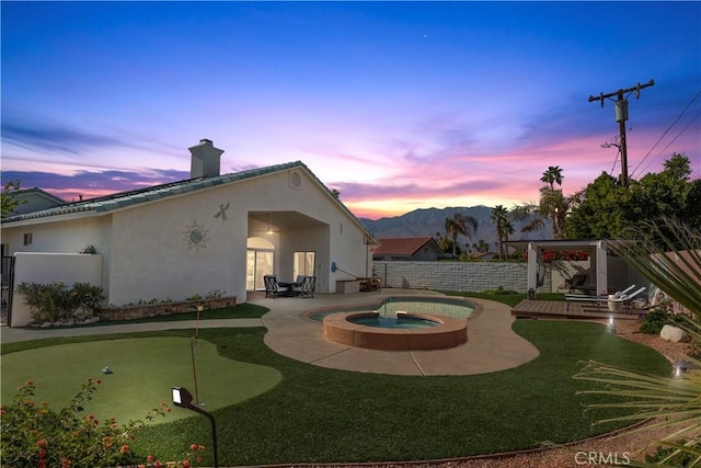 back house at dusk featuring a swimming pool with hot tub, a patio, and a mountain view