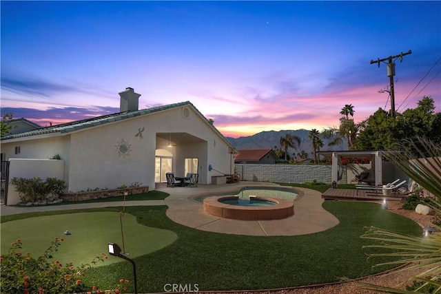 exterior space with a fenced backyard, a chimney, an in ground hot tub, a patio area, and stucco siding