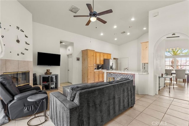 living room featuring a tile fireplace, light tile patterned floors, ceiling fan, and high vaulted ceiling