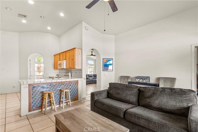 living area featuring light tile patterned floors, visible vents, arched walkways, ceiling fan, and high vaulted ceiling