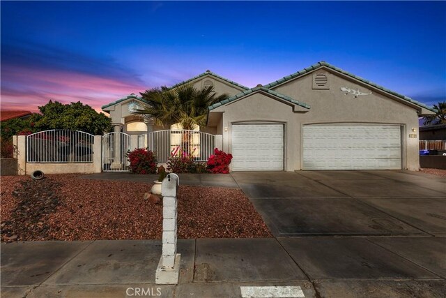 view of front of home with concrete driveway, a fenced front yard, an attached garage, a gate, and stucco siding