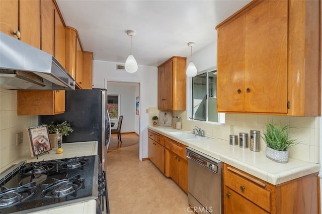 kitchen with tile countertops, sink, decorative backsplash, hanging light fixtures, and stainless steel appliances