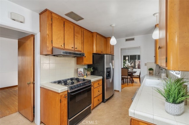 kitchen featuring pendant lighting, black gas range, tile counters, stainless steel fridge with ice dispenser, and decorative backsplash