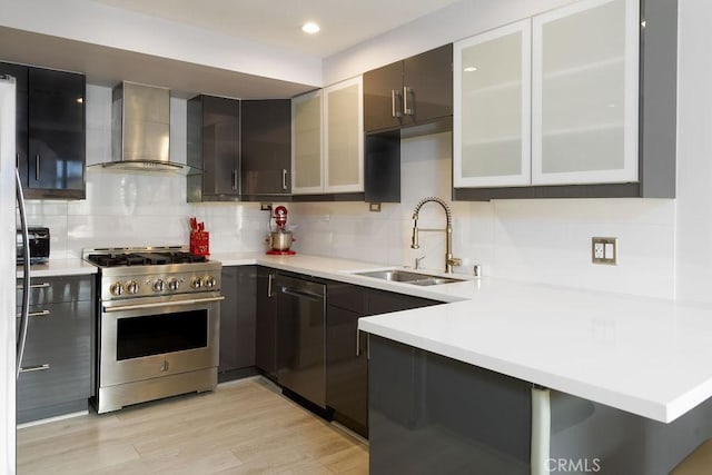 kitchen with high end stove, sink, decorative backsplash, kitchen peninsula, and wall chimney range hood