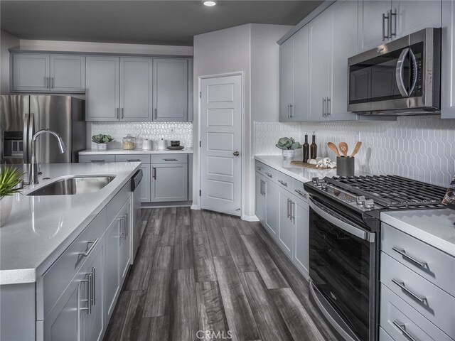 kitchen featuring gray cabinets, sink, backsplash, dark hardwood / wood-style flooring, and stainless steel appliances