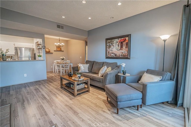 living room featuring sink, a chandelier, a textured ceiling, and light hardwood / wood-style floors