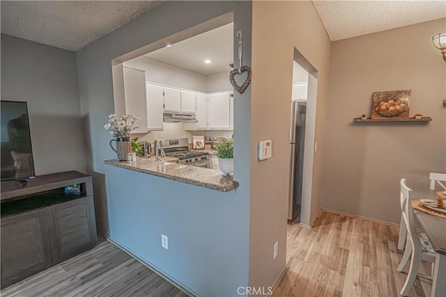 kitchen featuring appliances with stainless steel finishes, white cabinetry, light stone countertops, a textured ceiling, and light wood-type flooring