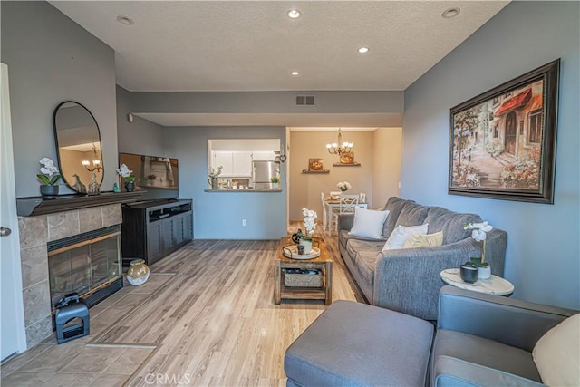 living room featuring a chandelier, a tiled fireplace, a textured ceiling, and light wood-type flooring