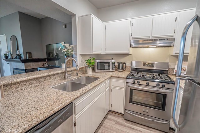 kitchen featuring appliances with stainless steel finishes, white cabinetry, sink, light stone counters, and light hardwood / wood-style floors