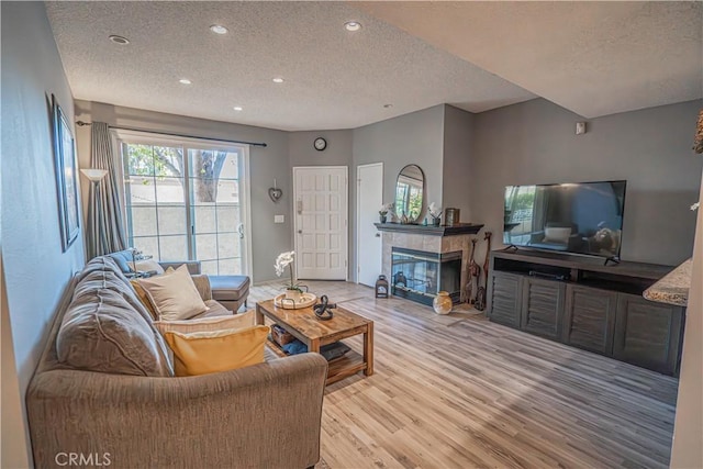 living room featuring a tiled fireplace, a textured ceiling, and light wood-type flooring