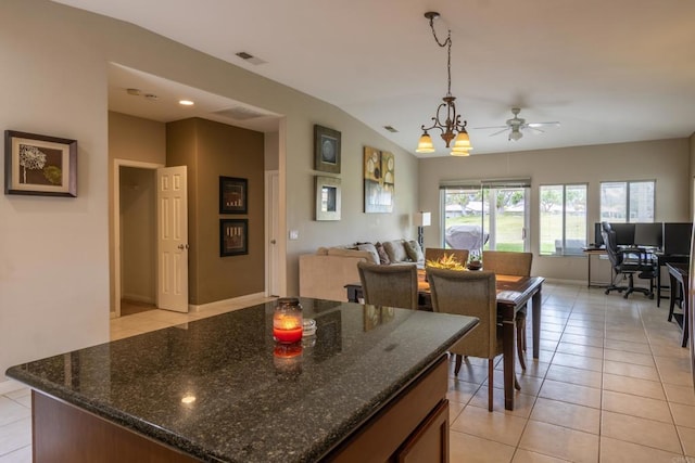 kitchen featuring ceiling fan with notable chandelier, pendant lighting, lofted ceiling, dark stone counters, and light tile patterned floors