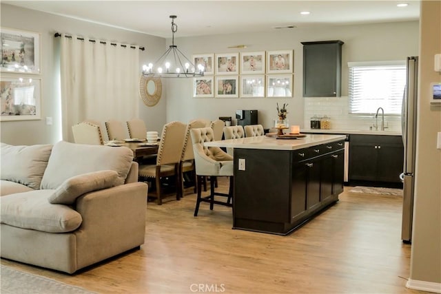 kitchen with a breakfast bar, sink, hanging light fixtures, light wood-type flooring, and a kitchen island