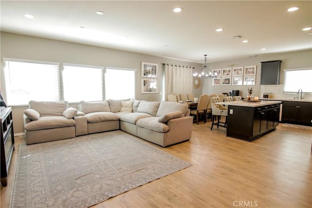 living room featuring sink, light hardwood / wood-style floors, a chandelier, and a healthy amount of sunlight