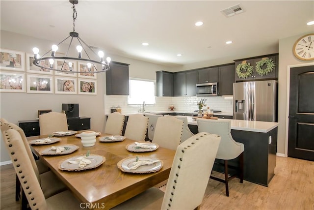 dining area with an inviting chandelier, sink, and light hardwood / wood-style flooring