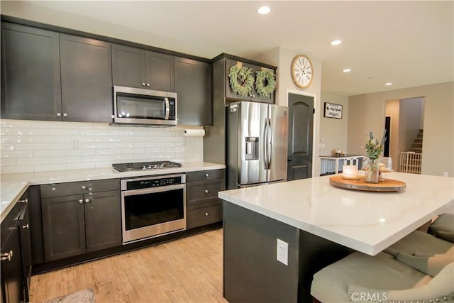 kitchen with a breakfast bar area, backsplash, a center island, stainless steel appliances, and light wood-type flooring