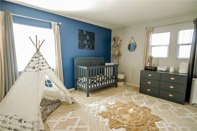 bedroom featuring light colored carpet and a nursery area