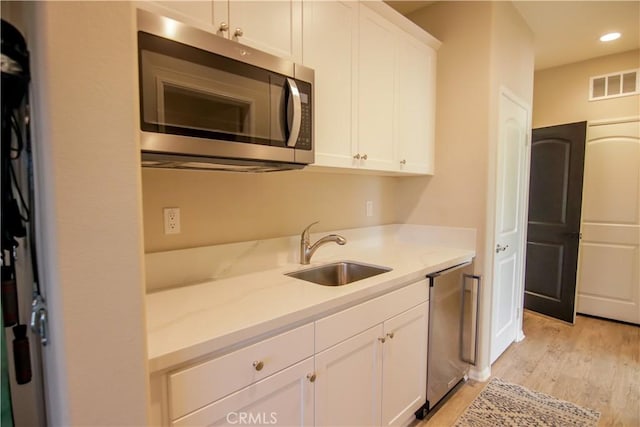 kitchen with sink, light hardwood / wood-style flooring, refrigerator, light stone countertops, and white cabinets