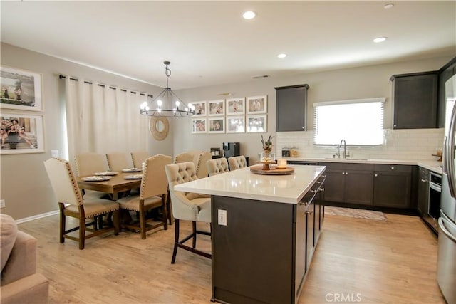 kitchen with sink, a kitchen breakfast bar, decorative backsplash, a kitchen island, and decorative light fixtures