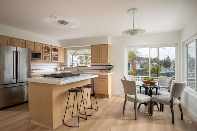 kitchen featuring tasteful backsplash, a center island, light wood-type flooring, tile counters, and stainless steel appliances