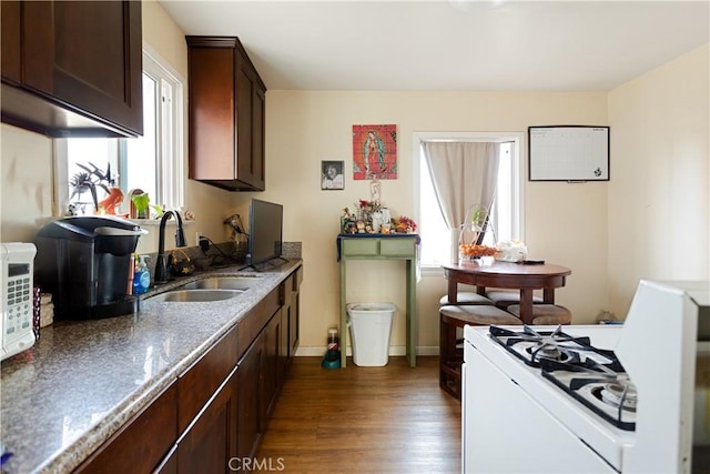 kitchen with dark hardwood / wood-style floors, sink, white range with gas cooktop, dark brown cabinetry, and light stone countertops