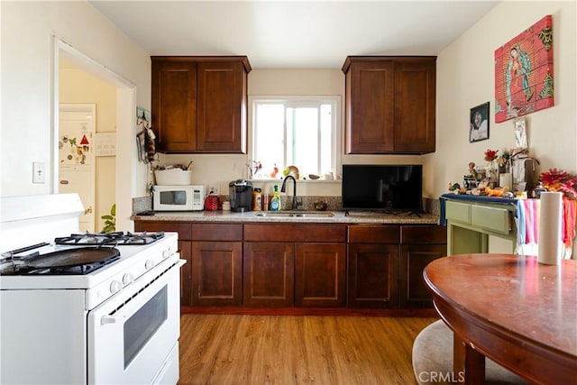 kitchen featuring white appliances, dark brown cabinetry, sink, and light wood-type flooring