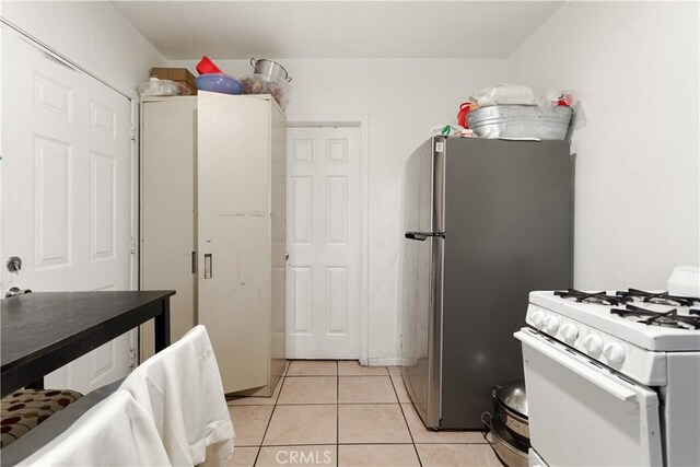 kitchen featuring light tile patterned flooring, white range with gas stovetop, and stainless steel fridge