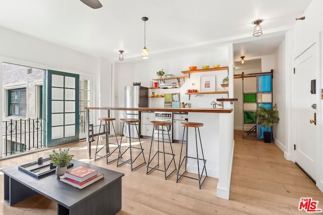 kitchen with a breakfast bar, pendant lighting, stainless steel fridge, a barn door, and light hardwood / wood-style flooring