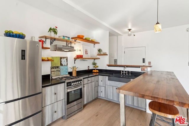 kitchen with appliances with stainless steel finishes, sink, hanging light fixtures, and light wood-type flooring