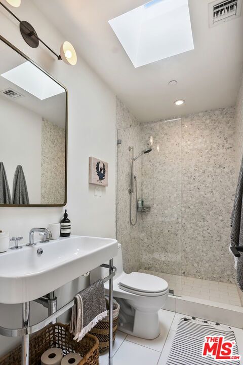 bathroom with tiled shower, tile patterned floors, toilet, and a skylight