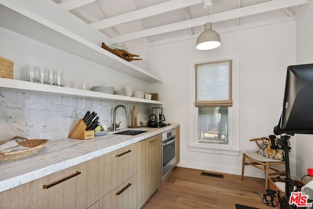 kitchen featuring sink, hanging light fixtures, light hardwood / wood-style flooring, beamed ceiling, and oven