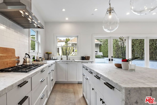 kitchen with island exhaust hood, stainless steel gas stovetop, a wealth of natural light, and white cabinets