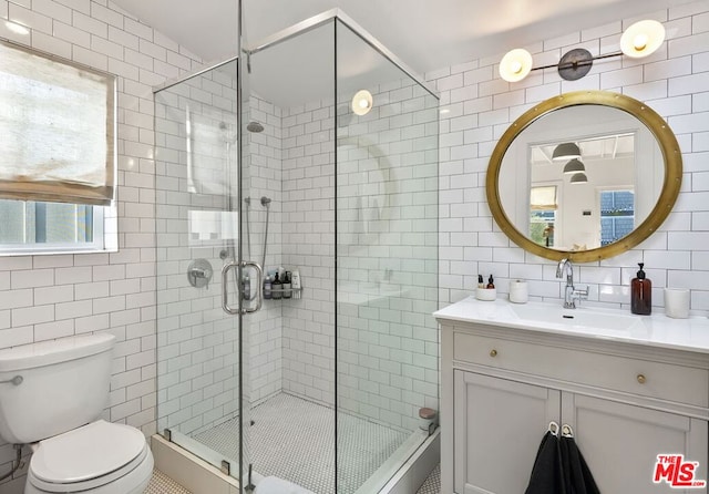 bathroom with a shower with door, vanity, tile walls, and toilet